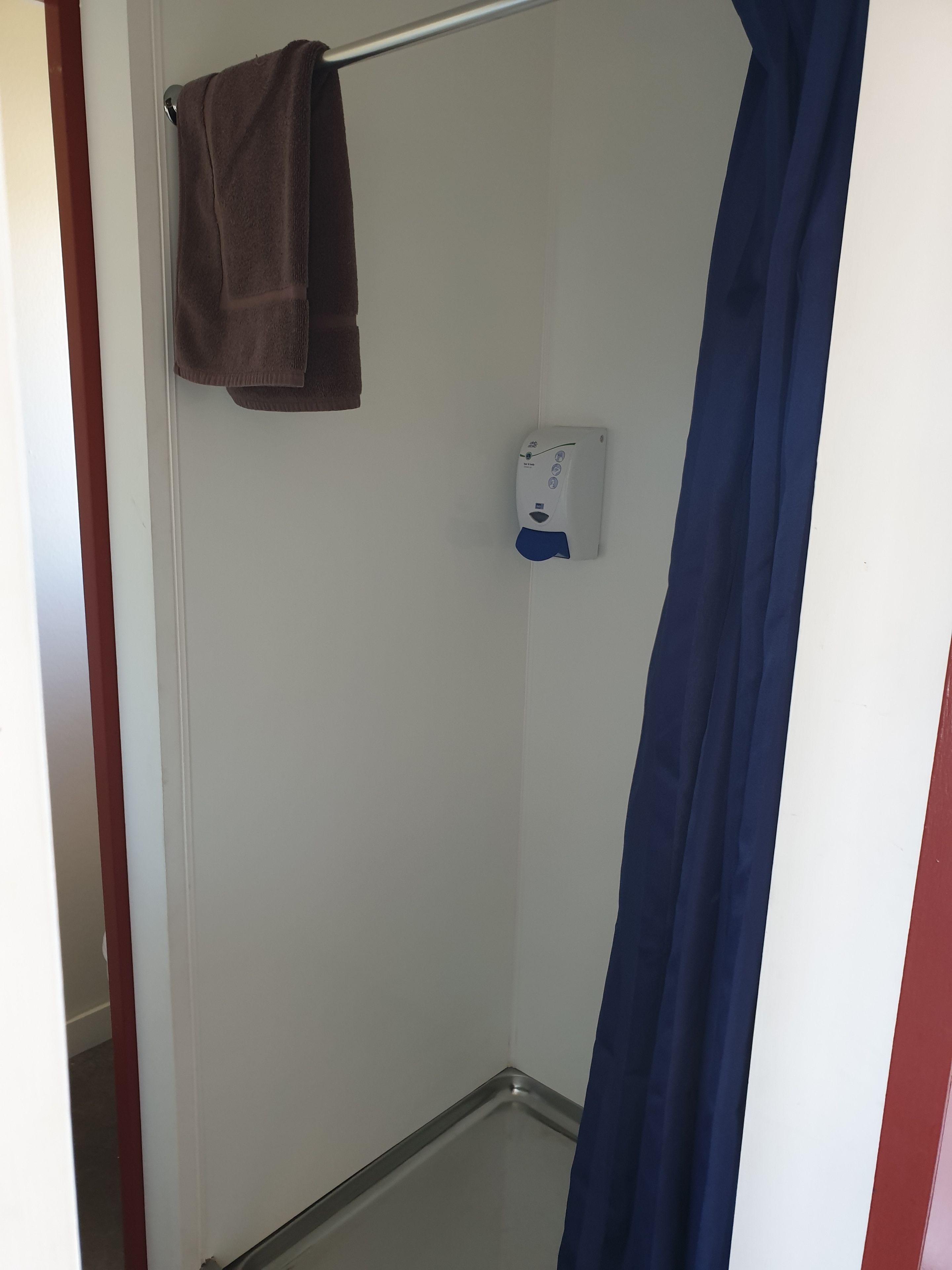 A small, enclosed shower area with a towel hanging on a rack, a soap dispenser mounted on the wall, and a blue shower curtain.