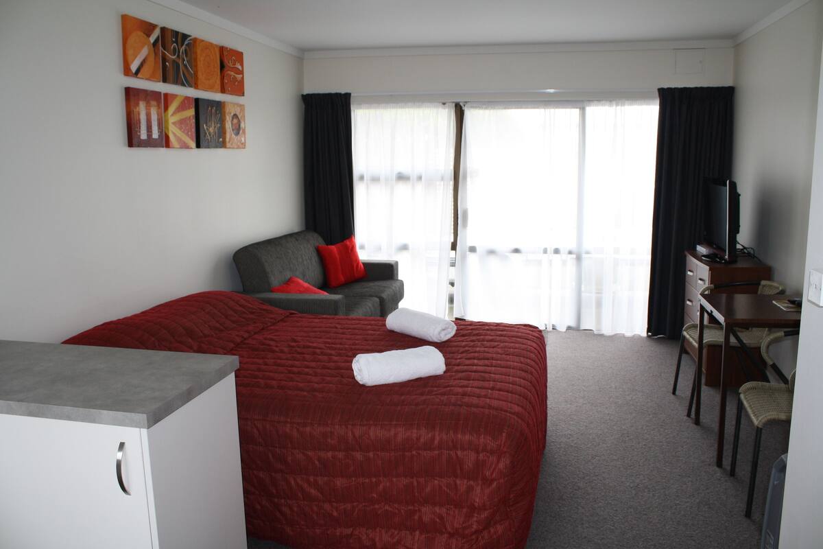 Ein Hotelzimmer mit Bett, Schreibtisch, Stuhl, Fernseher und einem Balkon mit Vorhängen.