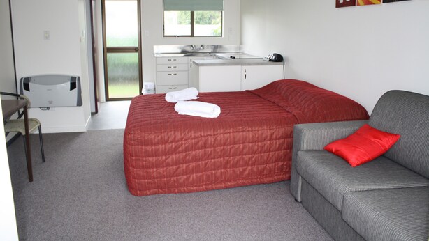 A bedroom with a bed, a sofa, a desk, and a window.