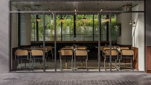 Un restaurante con fachada de vidrio, asientos en el interior y lámparas colgantes.