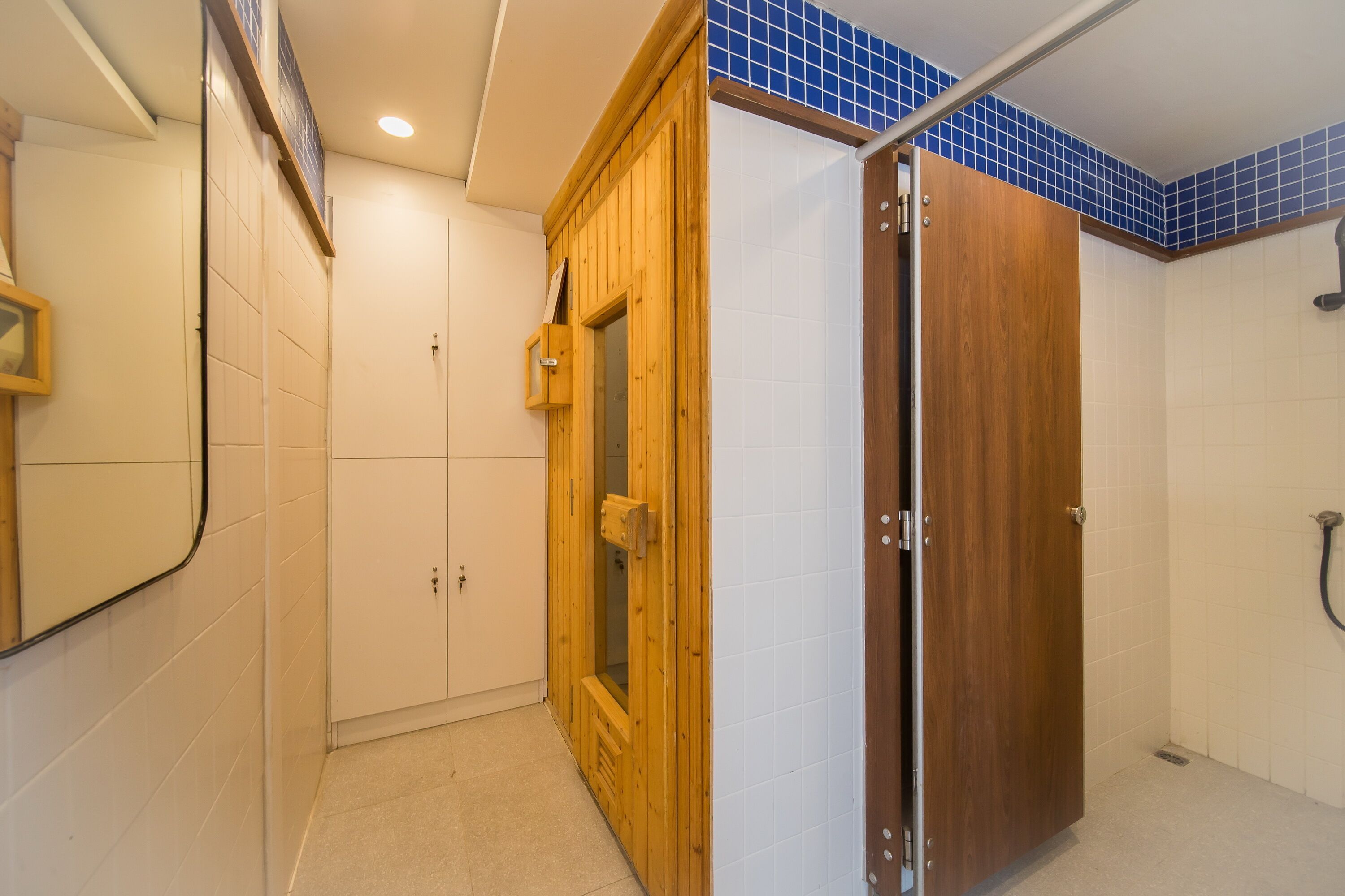 A bathroom with a wooden shower enclosure, a white tiled wall, and a wooden door.