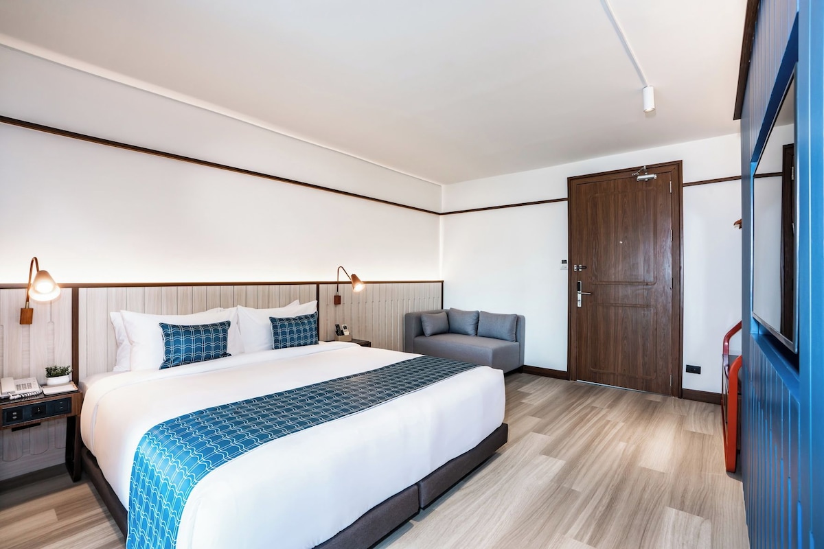 Habitación de hotel con una cama grande, lámparas de noche, un sofá, un armario y una puerta.