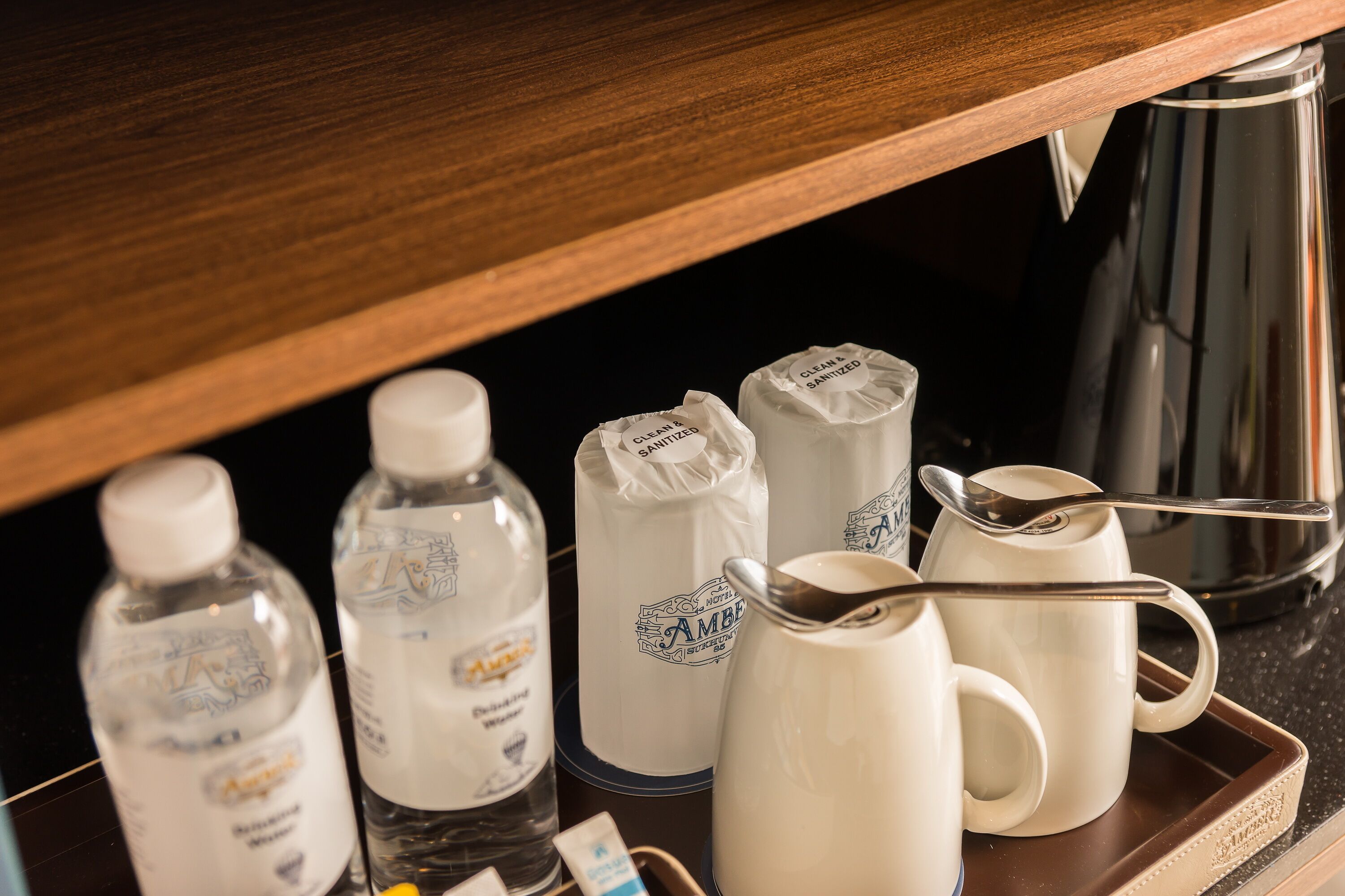 A tray with a water bottle, a jug, and a mug, along with a spoon and a kettle.