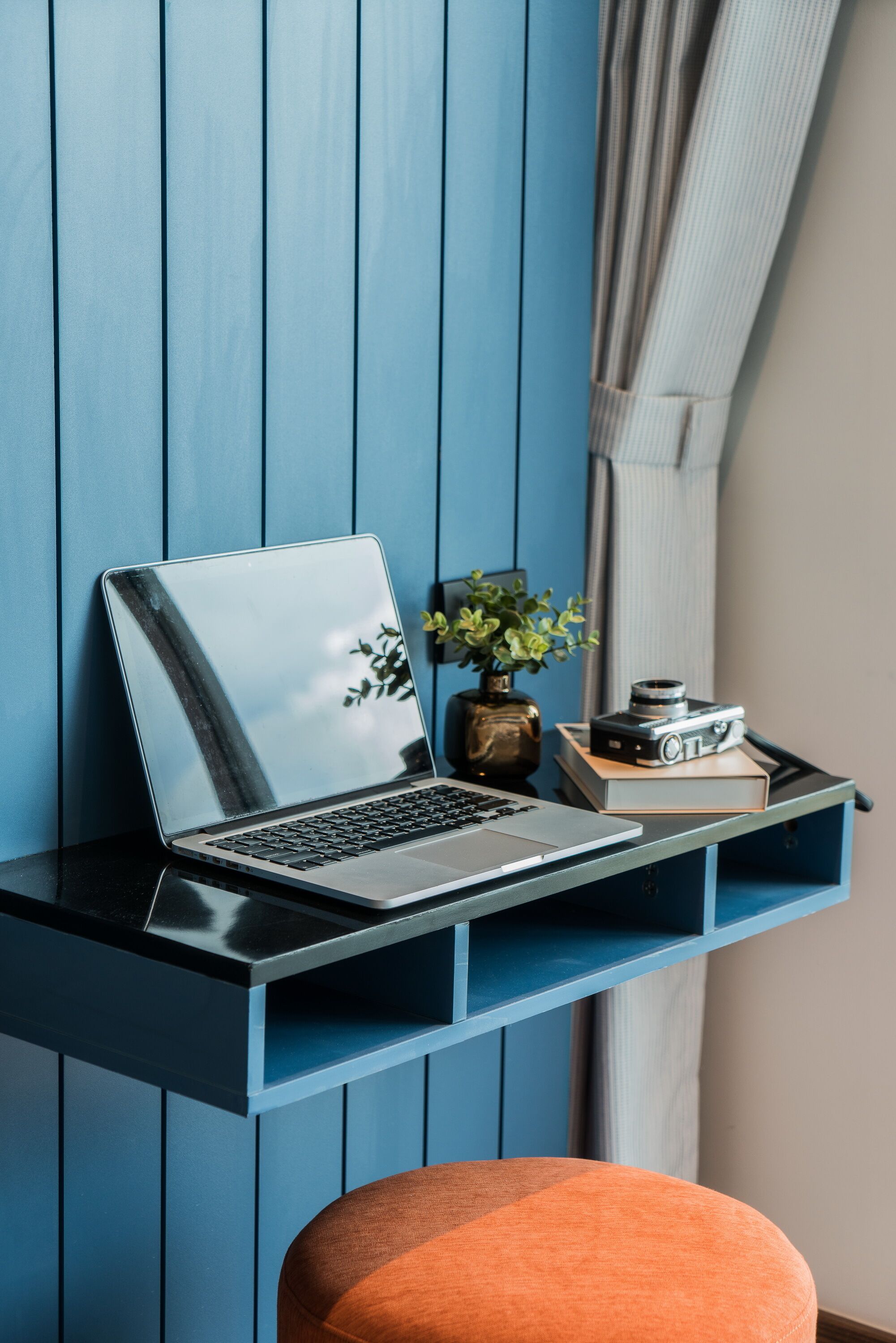 Un ordinateur portable sur un bureau noir, avec une plante et un appareil photo.