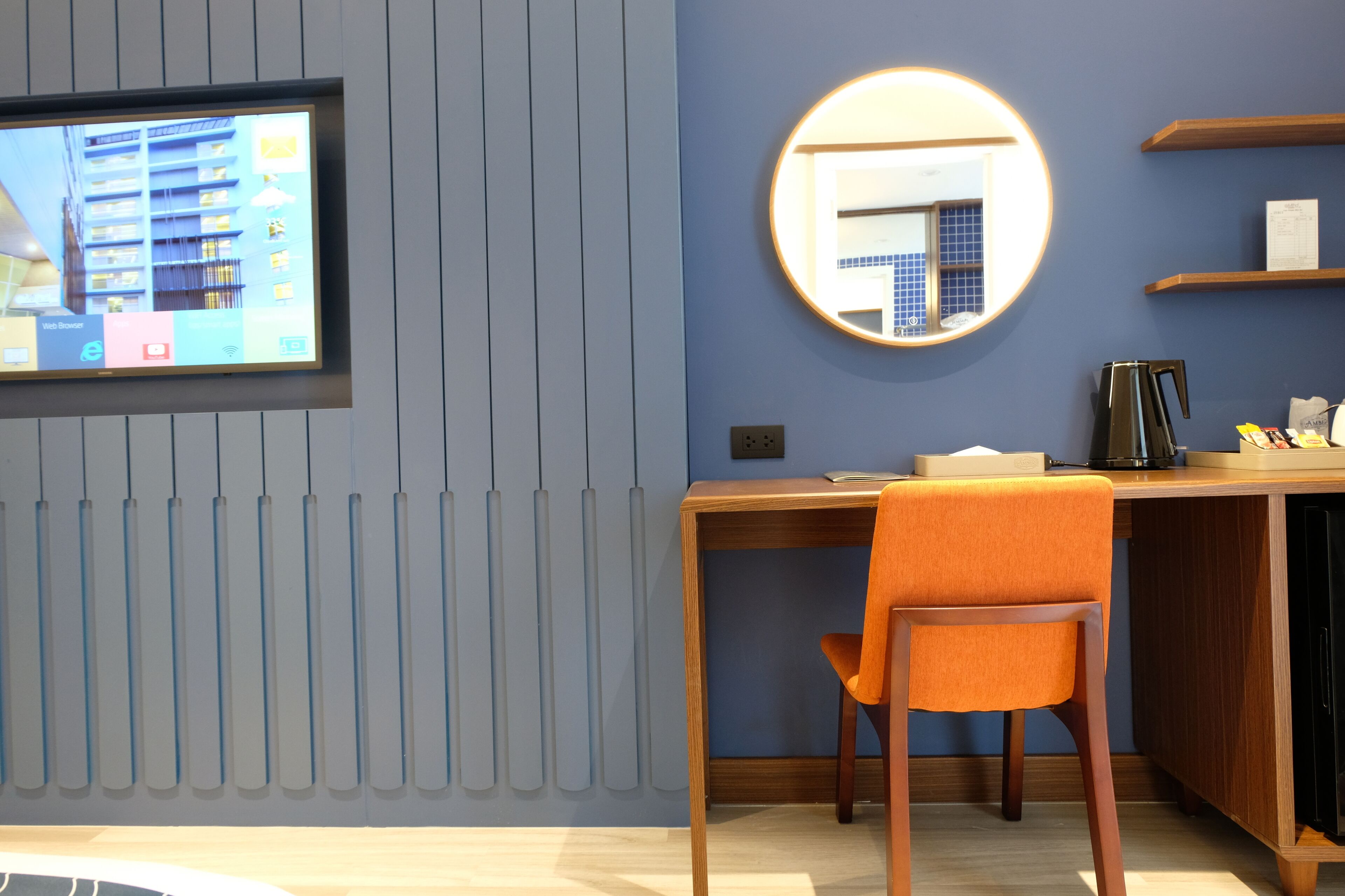 A modern room with a wooden desk, an orange chair, a round mirror, and a television mounted on the wall.