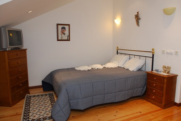 Un dormitorio con cama, cómoda, televisor encima de la cómoda, alfombra y lámpara fijada a la pared.