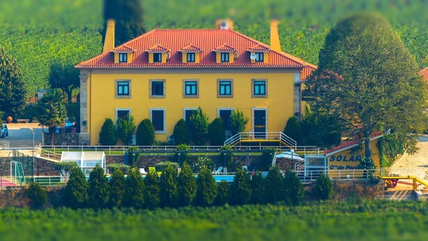 A yellow building with a red roof, surrounded by greenery and a solar panel installation. - Solar Quinta da Portela (Santa Marta de Penaguião)