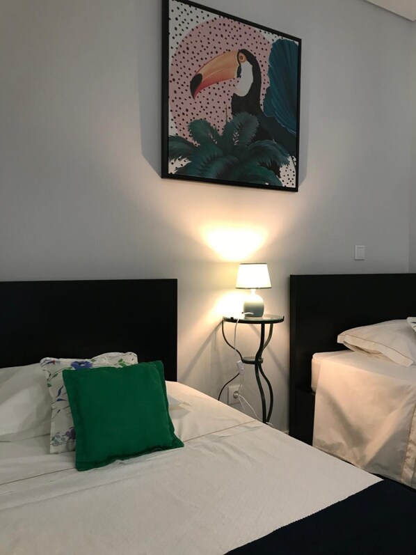 A hotel room with a bed, a nightstand with a lamp, and a wall-mounted painting of a toucan.