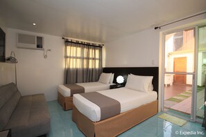 Habitación de hotel con dos camas, un sofá, un escritorio y una puerta corrediza de vidrio a un balcón.