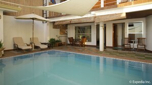 A swimming pool with lounge chairs and umbrellas, a covered patio area, and a view of the building's interior.
