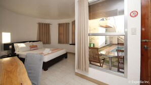A hotel room with a bed, a desk, a chair, and a view of an outdoor area with a pool and a staircase.