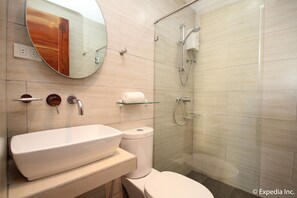 Un baño moderno con un espejo ovalado grande, un lavamanos blanco, un inodoro y una zona de ducha con mampara de cristal.