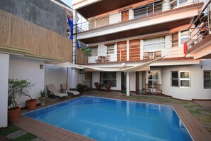 Un edificio de dos pisos con piscina, zona de estar al aire libre y un patio cubierto.