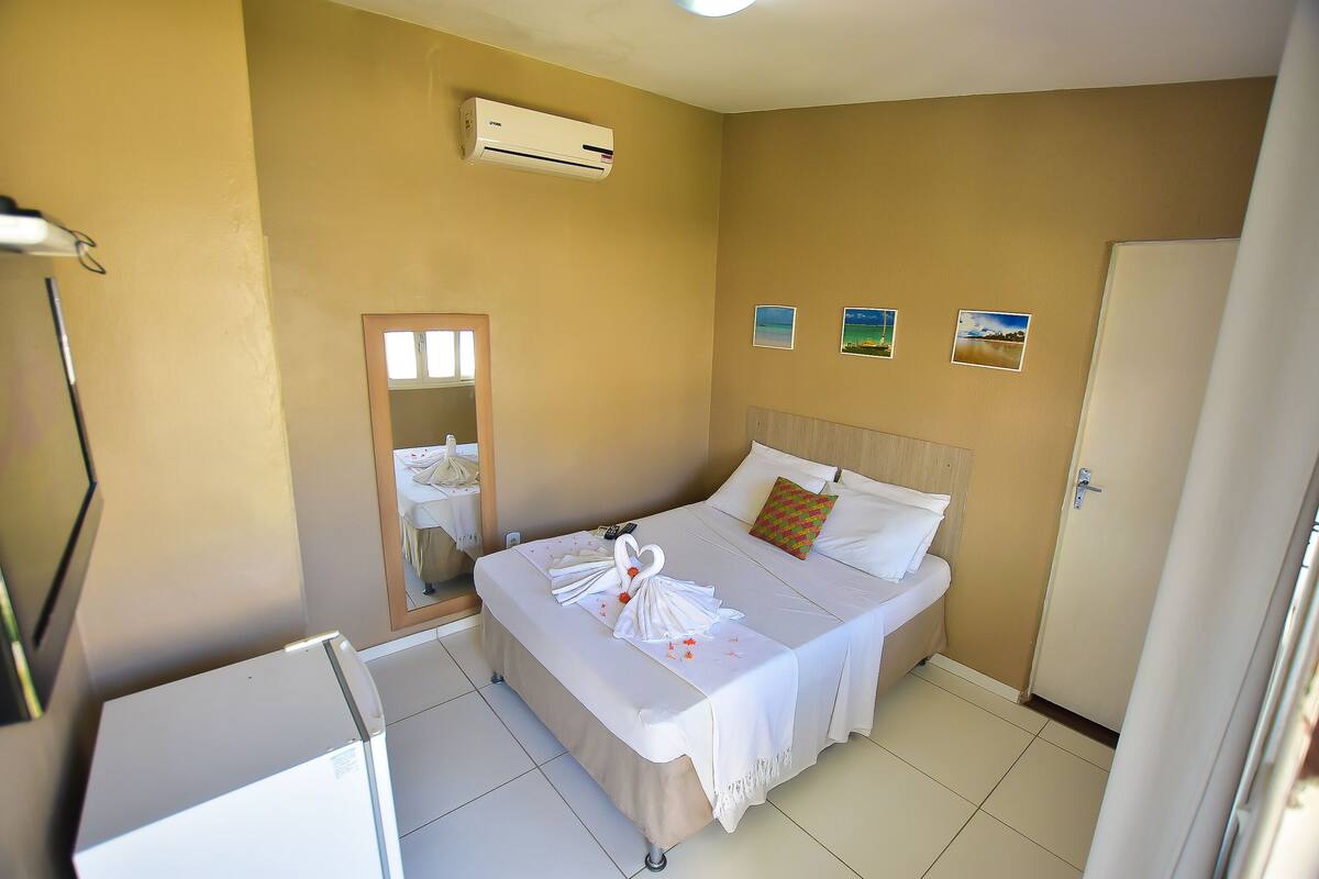 A hotel room with a bed, a mirror, an air conditioner, and a door.