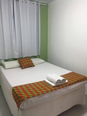 A single-bed room with a green wall, white curtains, and a patterned bedspread. - Pousada Vila Pajuçara (Maceió)