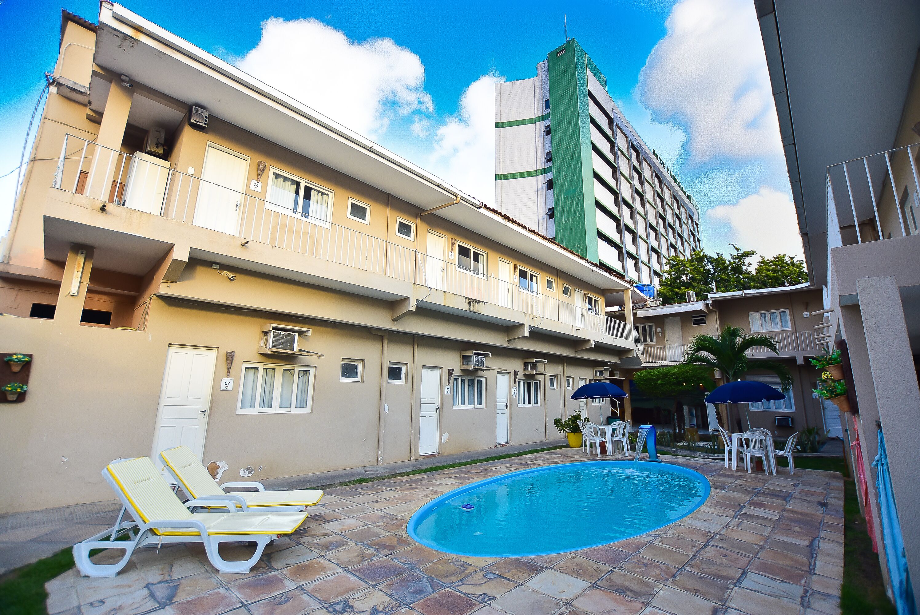 Edificio residencial con piscina, asientos al aire libre y un edificio alto contiguo.