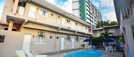 Edificio residencial con piscina, asientos al aire libre y un edificio alto contiguo.