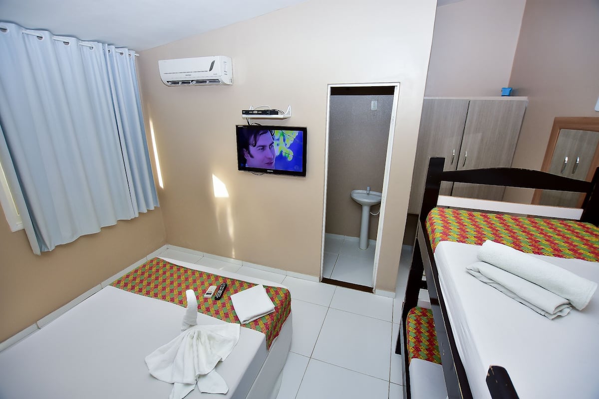 A hotel room with two beds, a television, an air conditioning unit, and a bathroom visible through an open door.