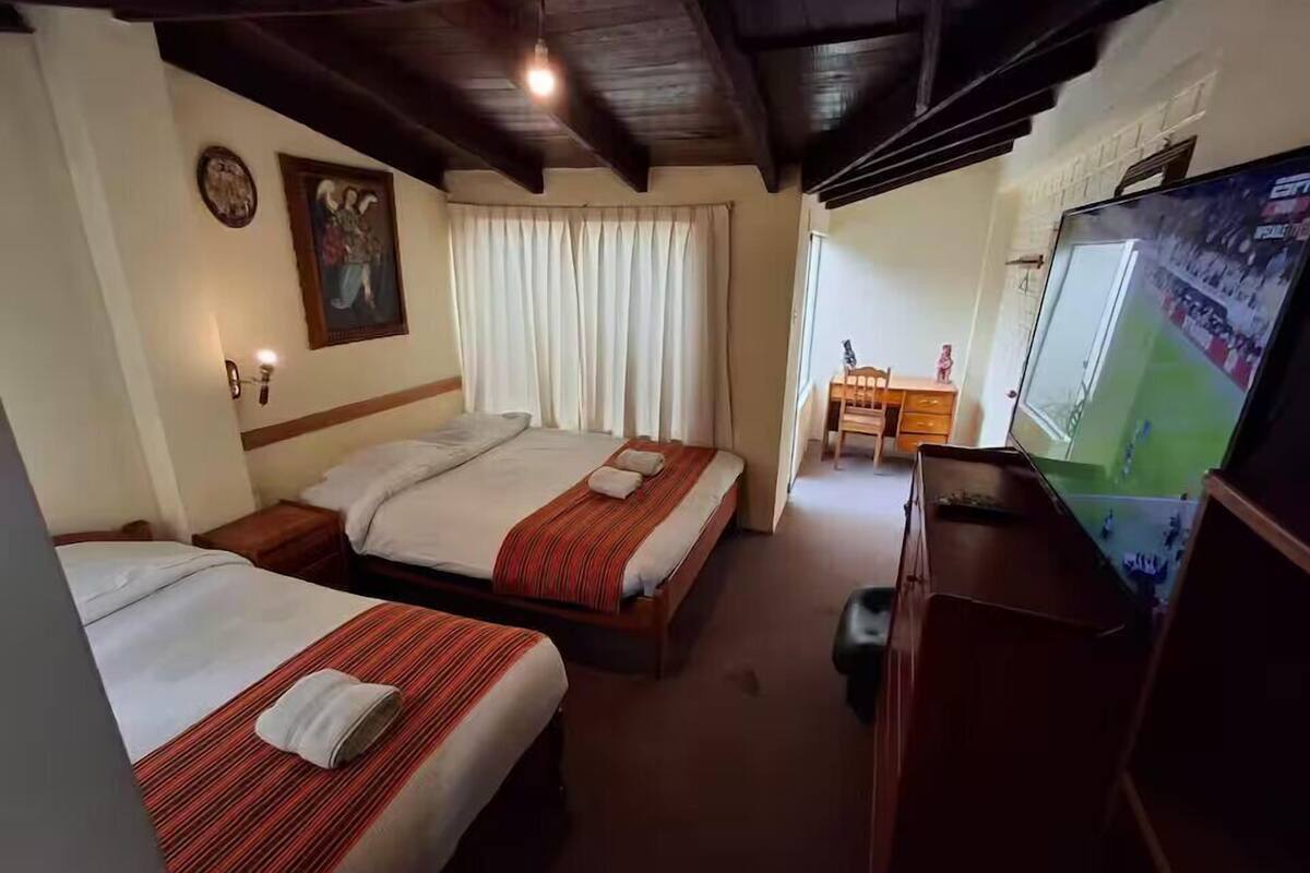 A hotel room with two beds, a desk, a television, and a window with curtains.