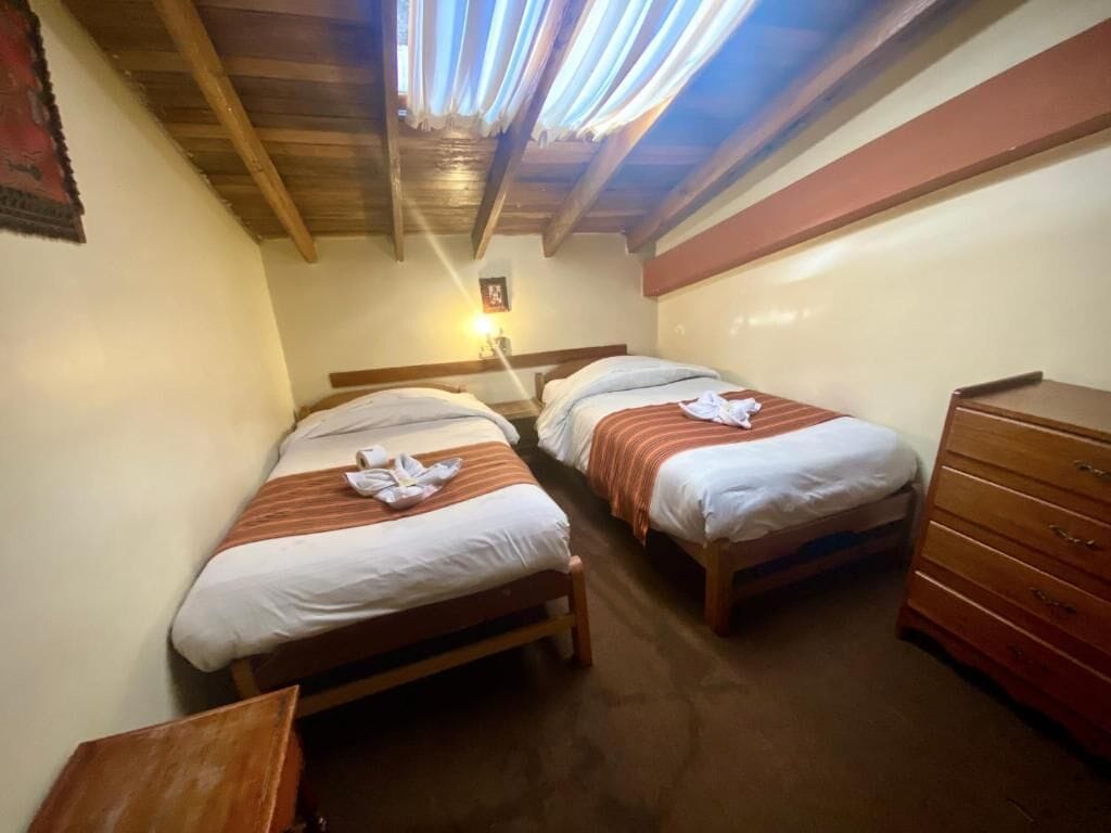 Una habitación pequeña y acogedora con dos camas individuales, un aparador de madera y un techo con vigas de madera.