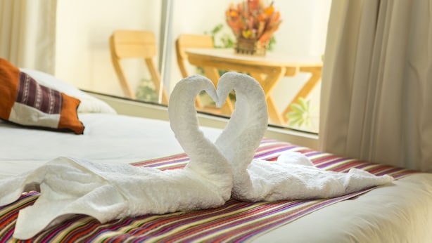 A bed with a towel arranged in the shape of a swan, a striped bedspread, and a window with a view of a dining area. - Andean Dreams Hotel (Cusco)