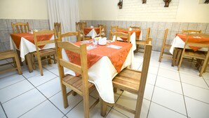 A dining area with wooden tables and chairs, each covered with a white tablecloth and orange napkins. - Andean Dreams Hotel (Cusco)