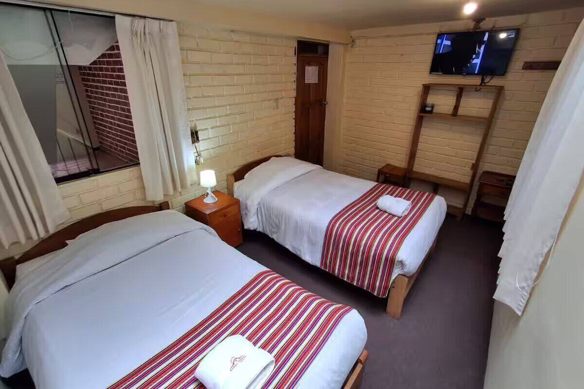 A hotel room with two beds, a TV on the wall, and a window with curtains.
