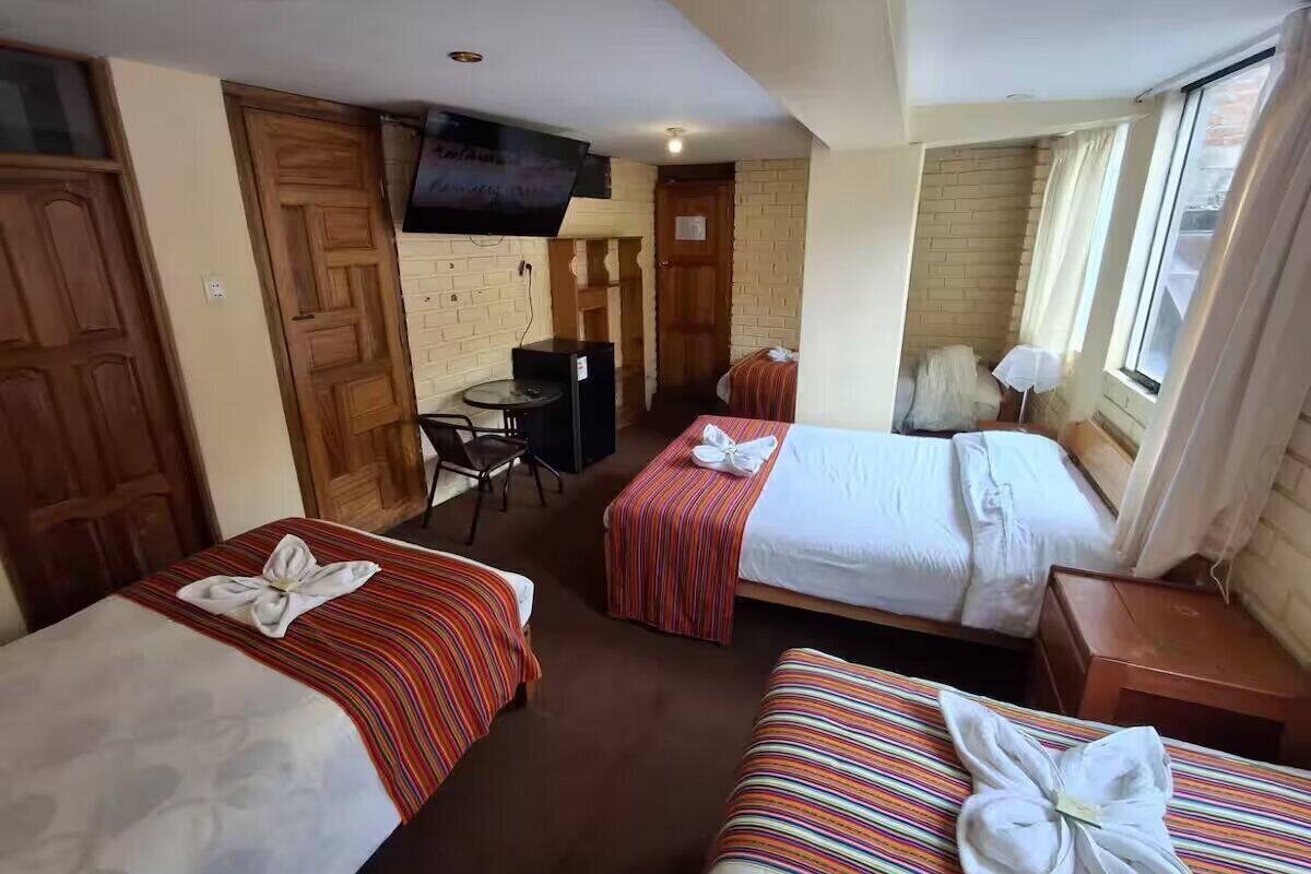 A hotel room with two beds, a TV, a small desk, and a window with curtains.