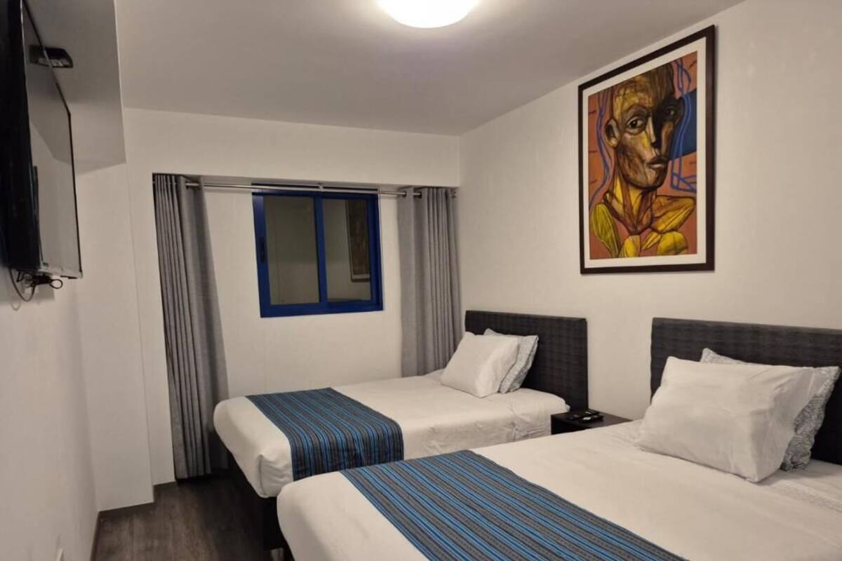 A hotel room with two beds, a window with curtains, a painting on the wall, and a TV on the left.