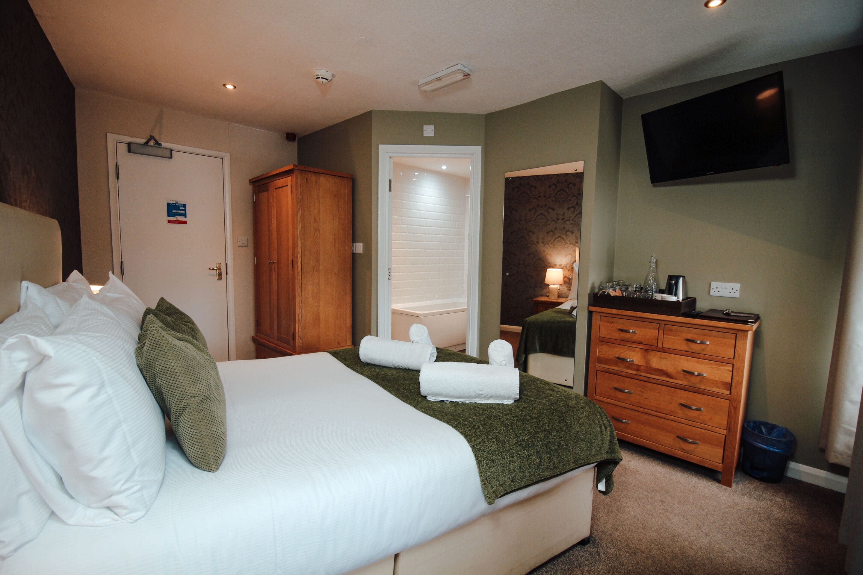 Une chambre d’hôtel avec un lit, une armoire en bois, une commode, un téléviseur et une porte de salle de bain.