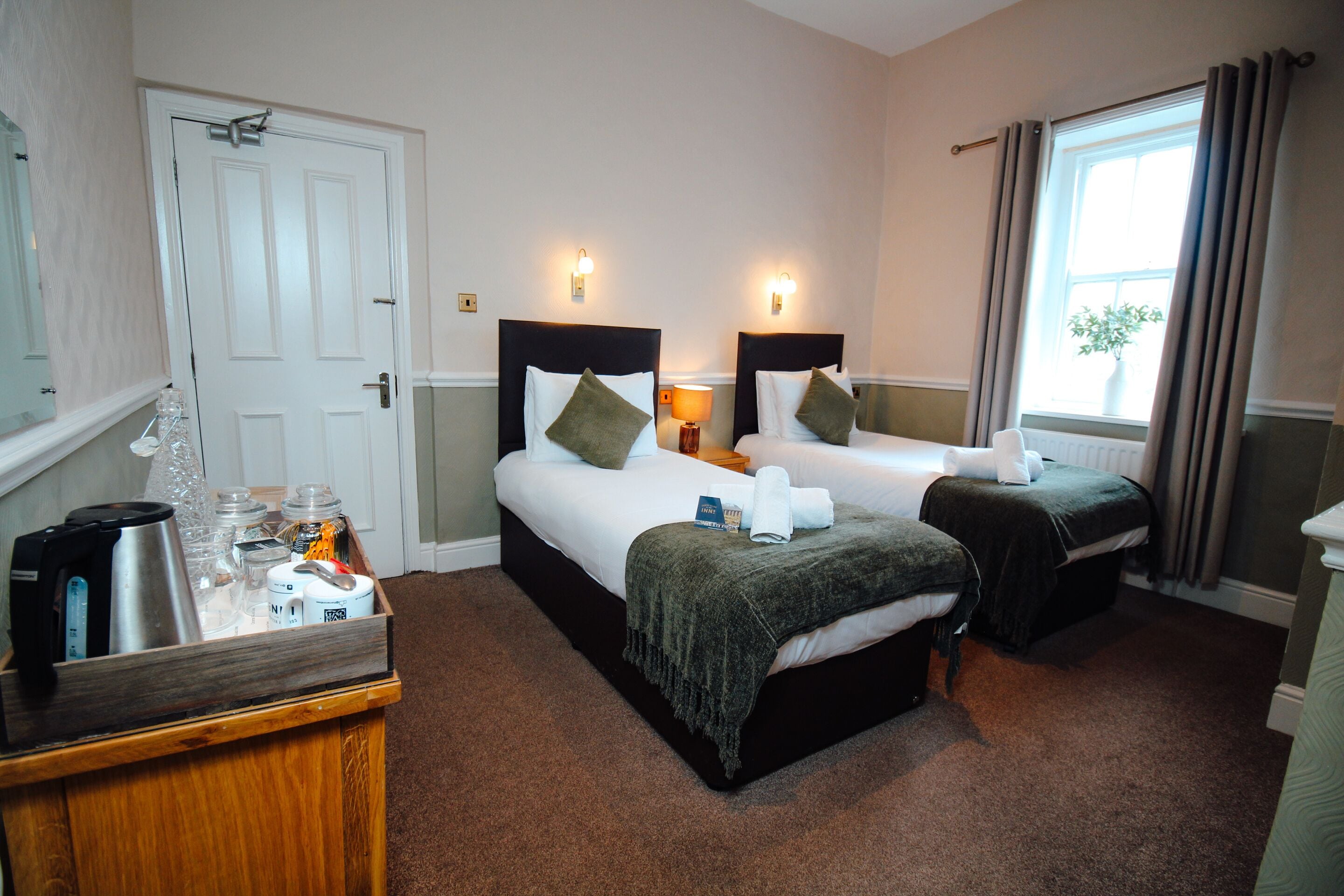 A hotel room with two beds, a coffee maker, and a tray of breakfast items.