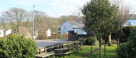 A picnic area with benches and picnic tables, surrounded by greenery and a stone wall.