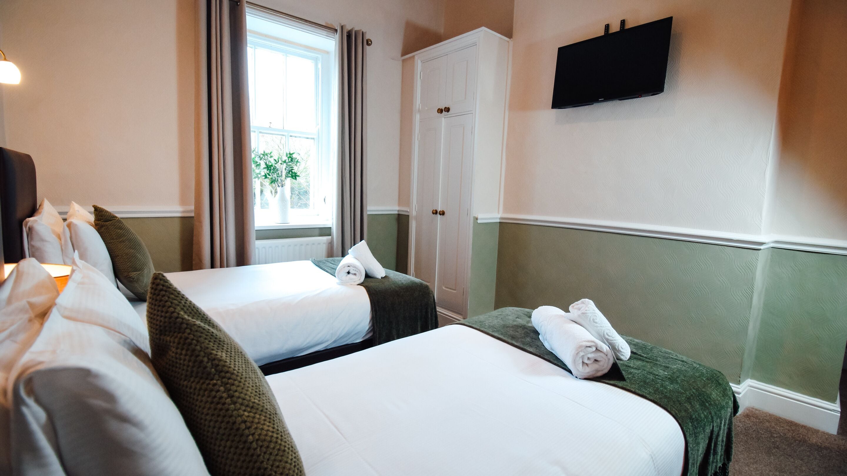 Een hotelkamer met twee bedden, een kledingkast, een televisie en een raam met gordijnen.
