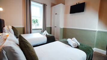 Een hotelkamer met twee bedden, een kledingkast, een televisie en een raam met gordijnen.