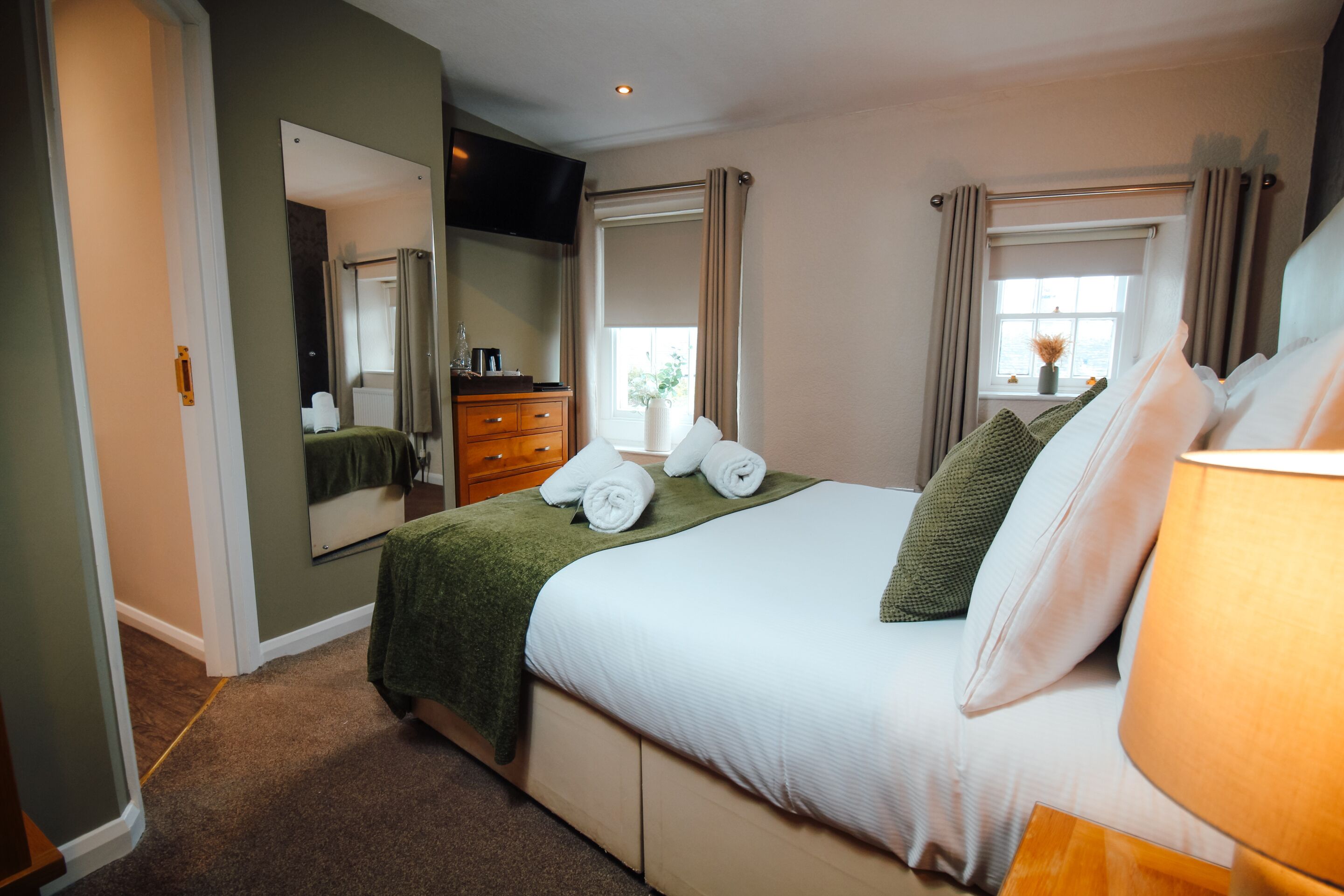 A hotel room with a bed, a dresser, a mirror, a TV, and a window with curtains.