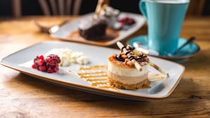 Ein Dessertteller mit mehrschichtiger Torte, Beeren und Karamellsauce auf einer Holztischplatte.