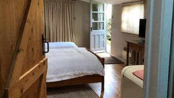 A bedroom with a wooden bed, a bedside table, a chair, a window with curtains, and a door leading outside.