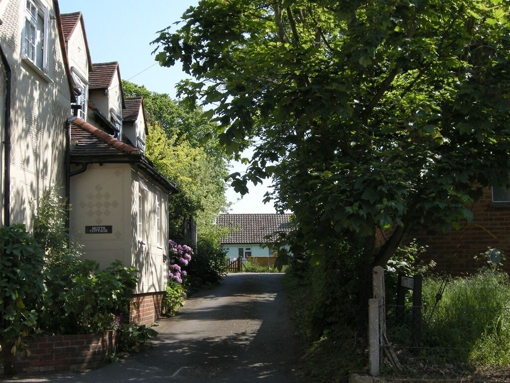 Een smalle woonstraat met huizen aan beide kanten, een bord met de tekst 'MOTTER COTTAGE' en een boom die schaduw geeft.