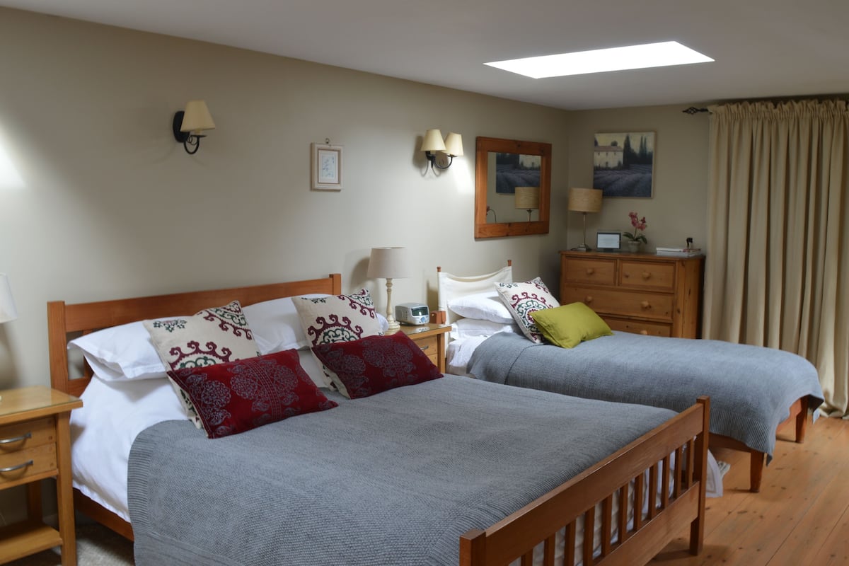 A hotel room with two single beds, a wooden nightstand with a lamp, a dresser, and a painting on the wall.