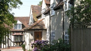 A traditional two-story house with a steeply pitched roof, a wooden door, and a small window. - Motts Cottage (Dunmow)