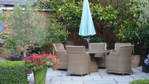An outdoor patio with wicker furniture, a blue umbrella, and various potted plants. - Motts Cottage (Dunmow)