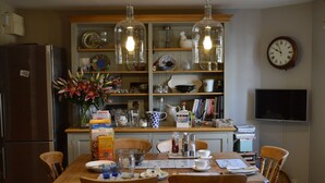 A dining area with a wooden table, chairs, and a kitchen in the background. - Motts Cottage (Dunmow)