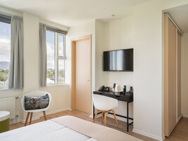Una habitación de hotel moderna con una cama, un escritorio con silla, un televisor en la pared y una ventana con cortinas.