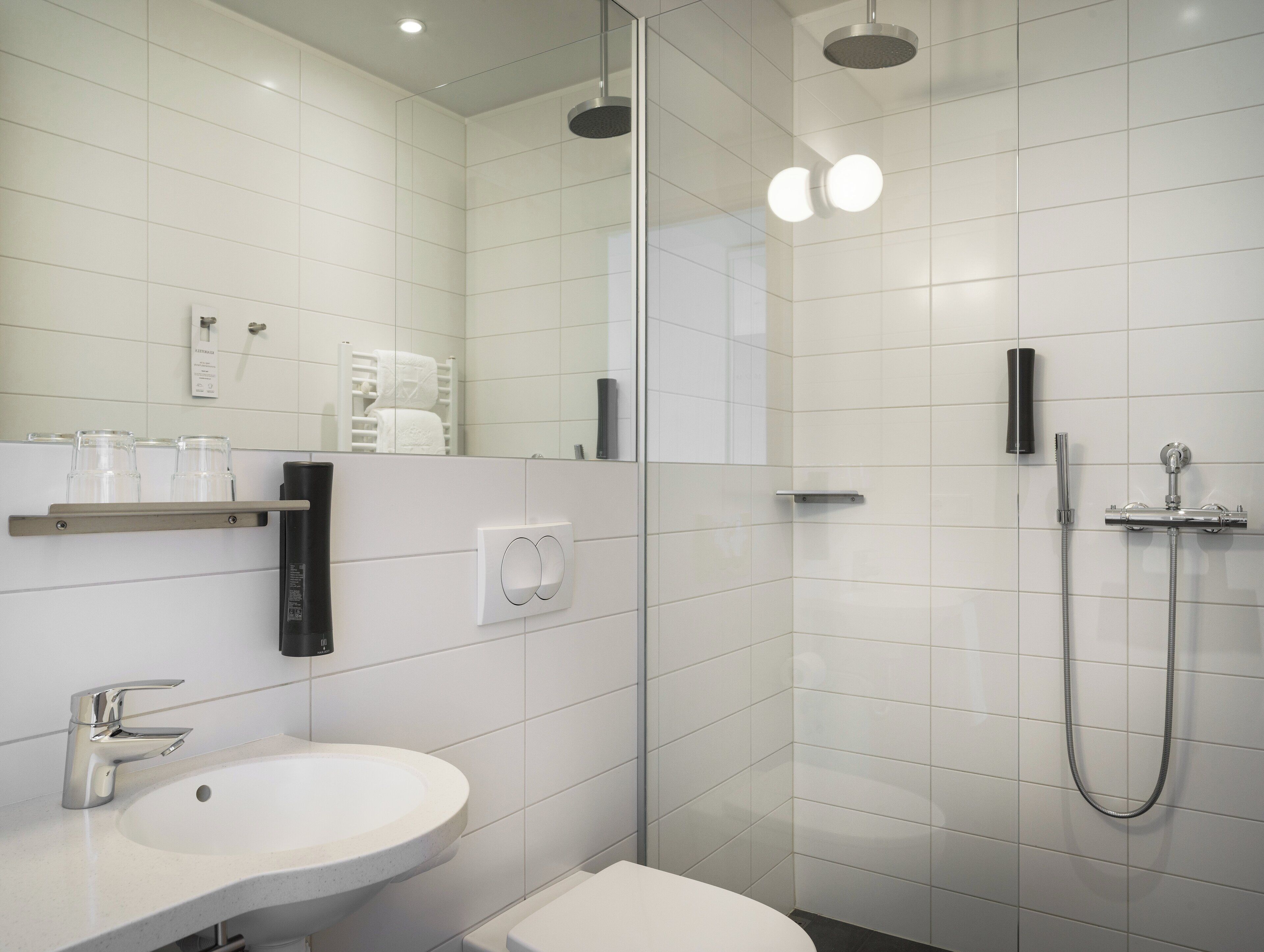 A modern bathroom with a white sink, a toilet, a glass shower enclosure, and a mirror.