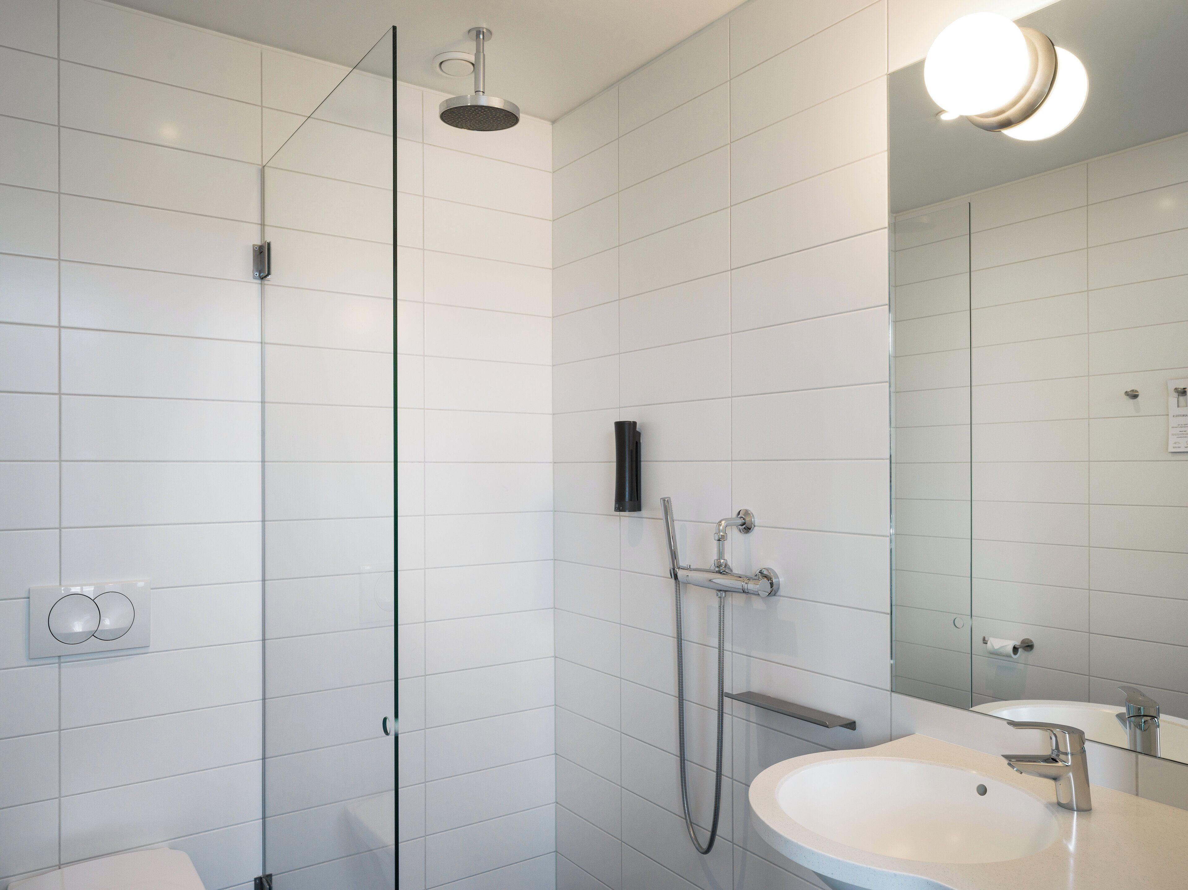 A modern bathroom with a glass shower enclosure, a white sink, and a mirror.