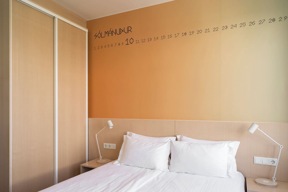 A hotel room with a bed, two bedside tables, and a wall with numbers and the word "SOLUMANUXUR".