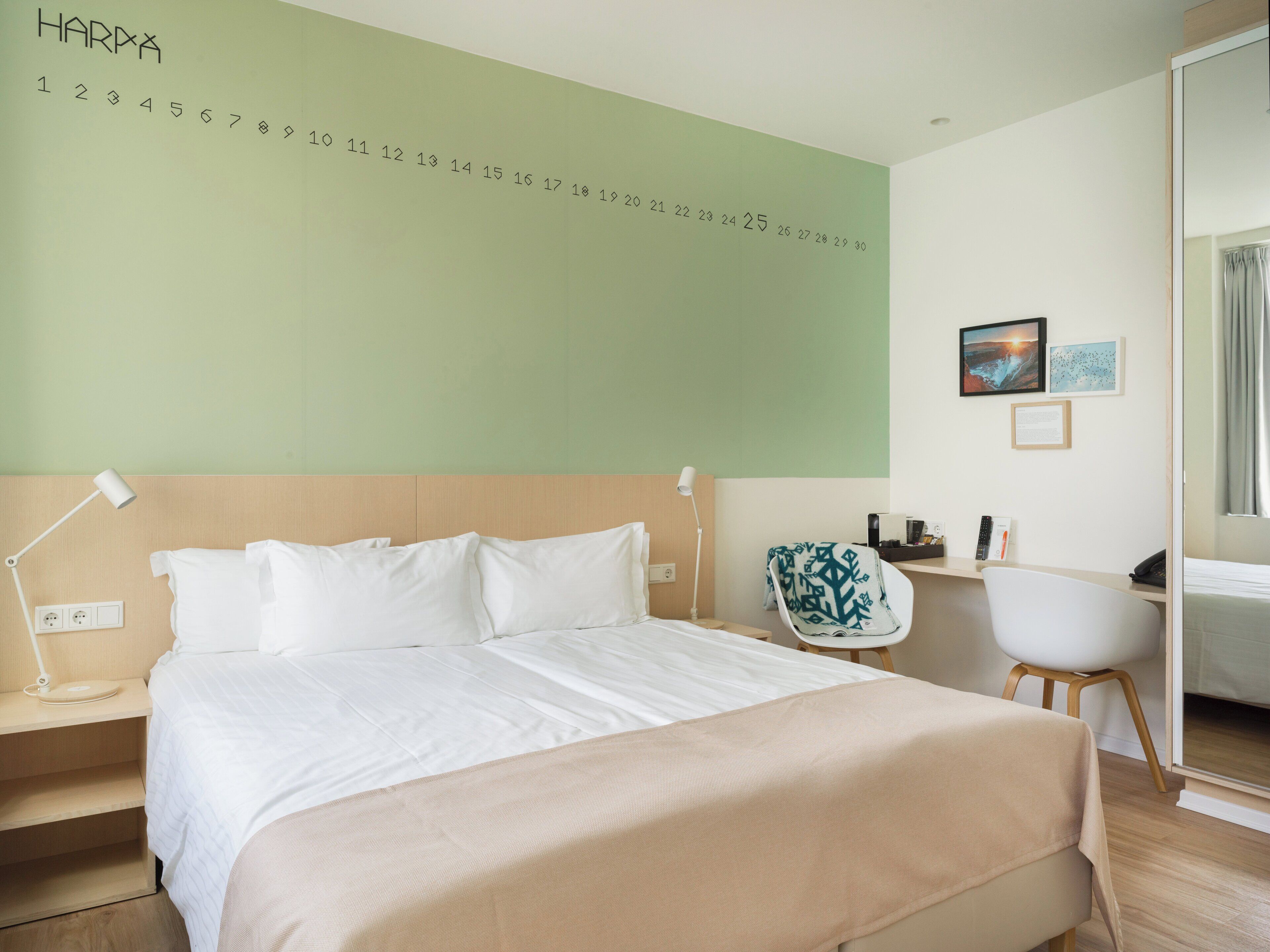 A hotel room with a bed, a desk, a chair, a nightstand, and a wall calendar.