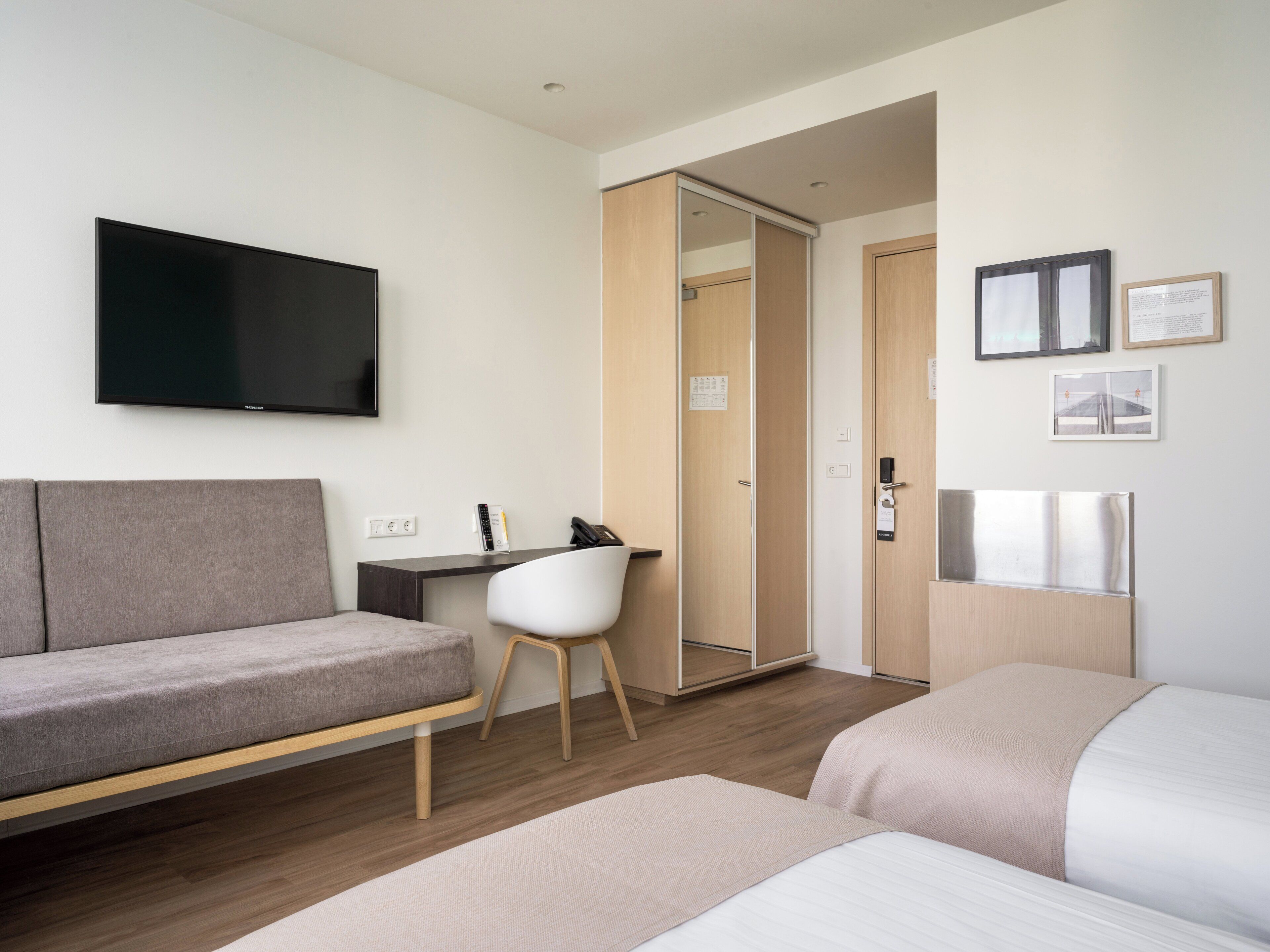 A modern hotel room with a sofa, a desk, a chair, a bed, and a TV.