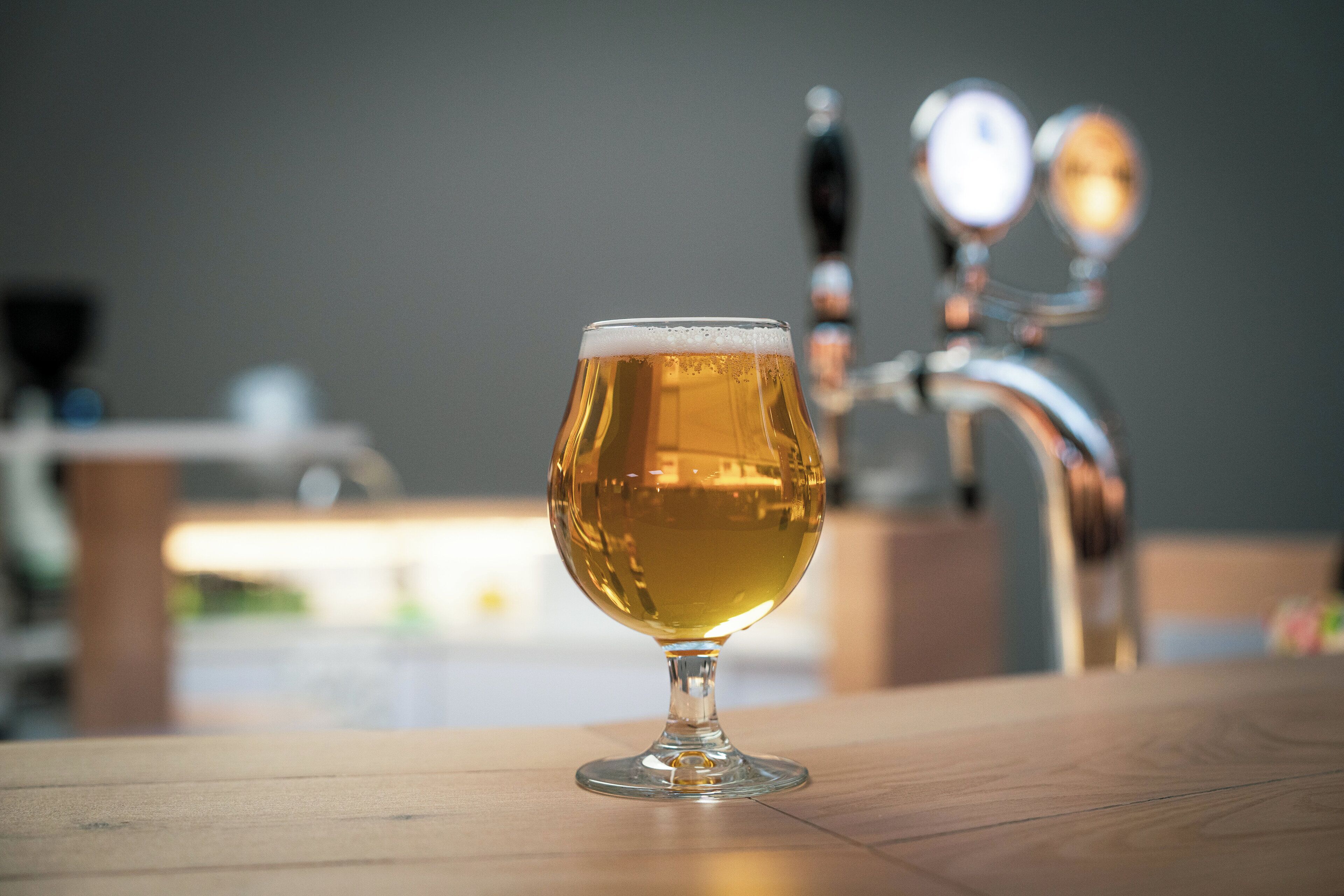 A glass of beer on a wooden table with a blurred background of a bar area.