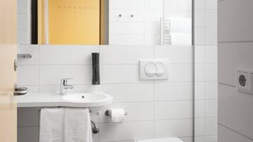 A modern bathroom with a white sink, toilet, and mirror. There is a towel hanging on the wall and a soap dispenser.